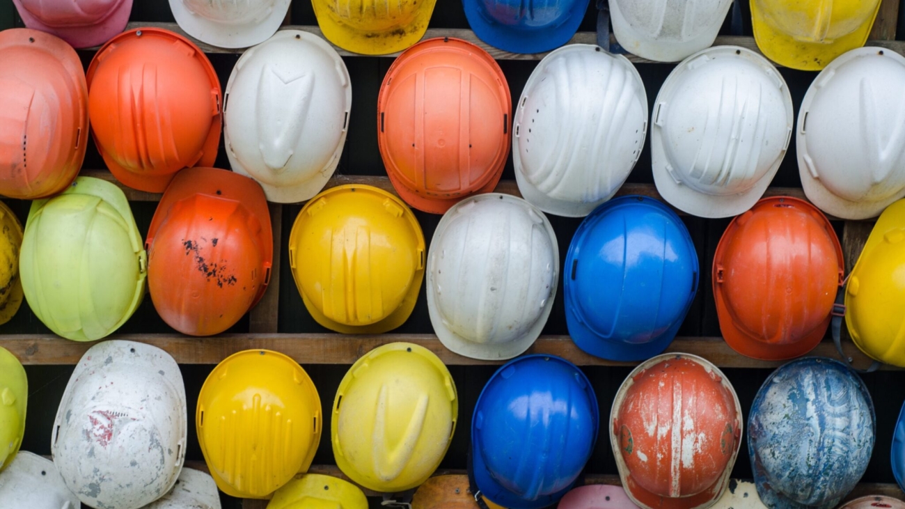 A wall of hardhats that are different colors, white, yellow, blue and red