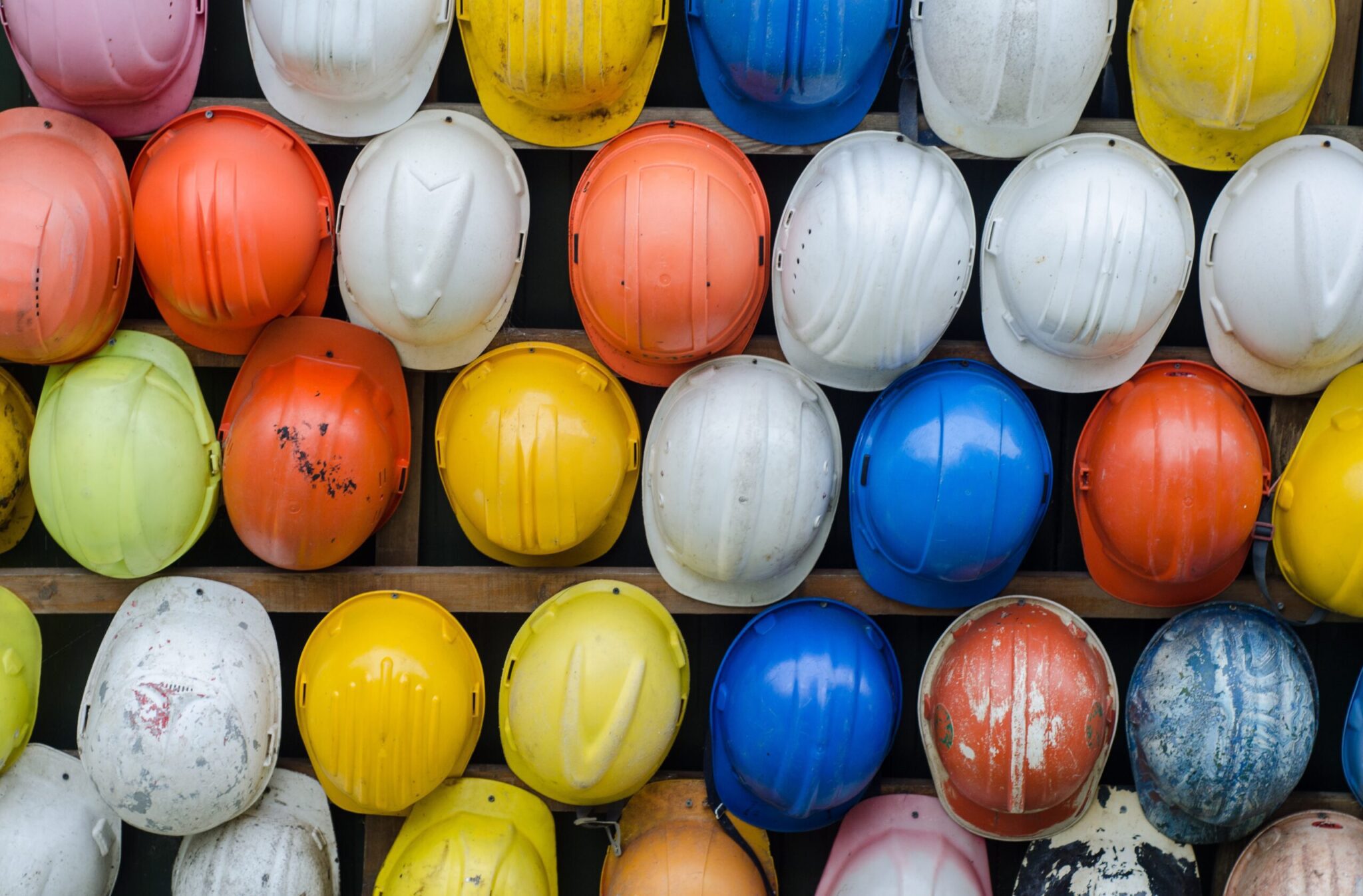 A wall of hardhats that are different colors, white, yellow, blue and red