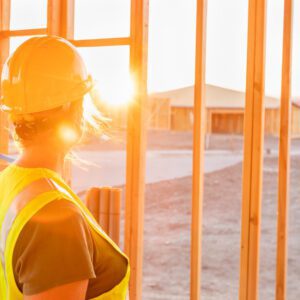 Female Construcion Worker Looking Out From New Home Framing with the sun shining