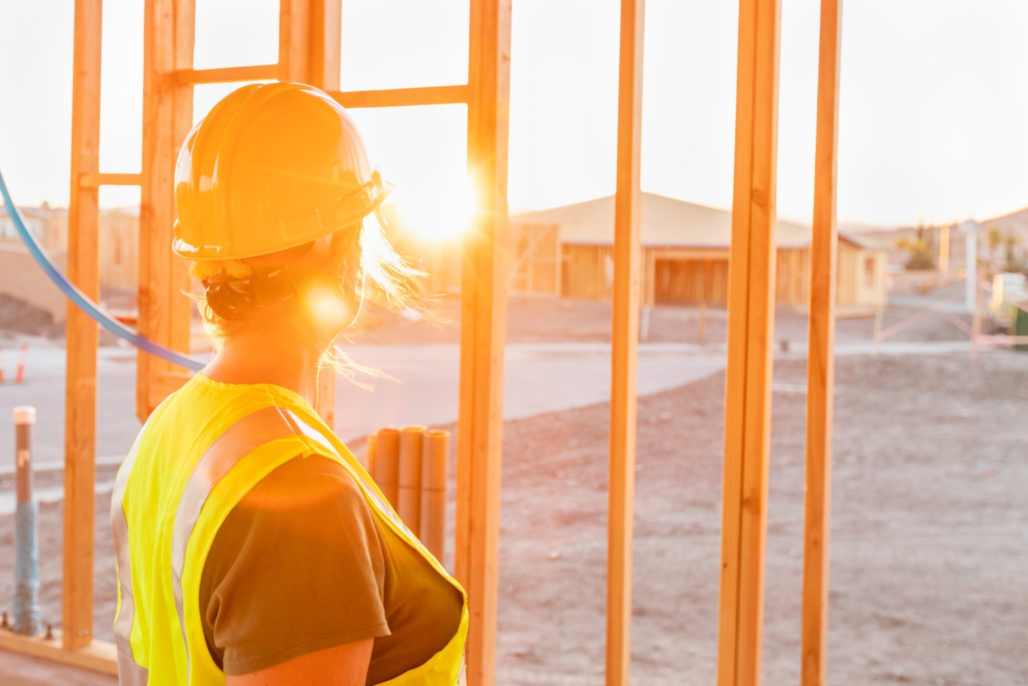 Female Construcion Worker Looking Out From New Home Framing with the sun shining