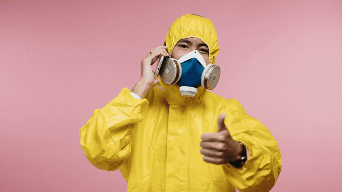 Man wearing yellow coveralls and respirator against pink background