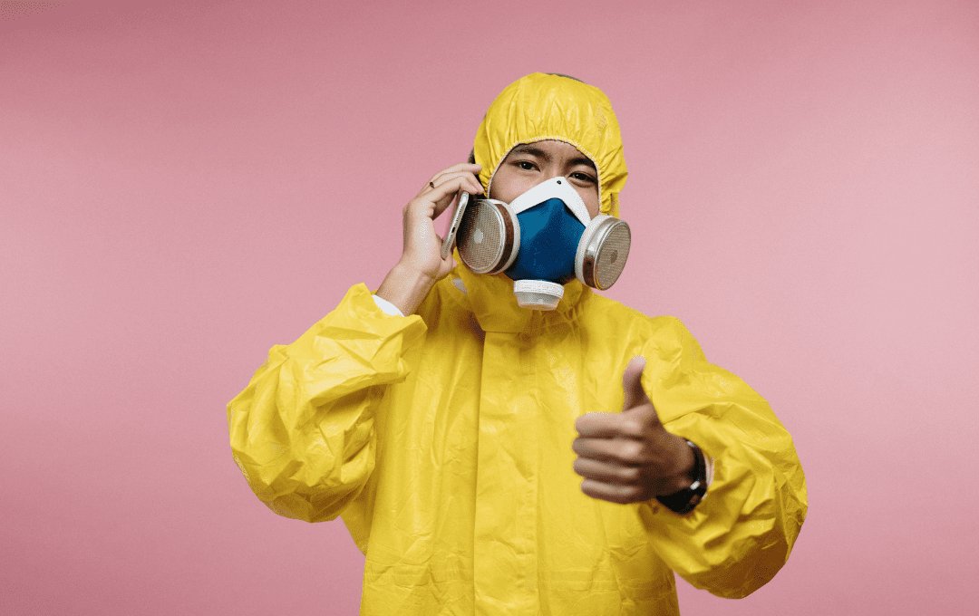 Man wearing yellow coveralls and respirator against pink background