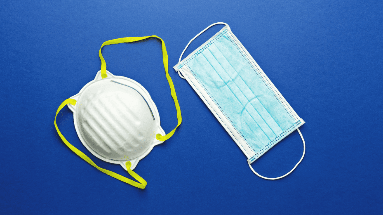 A white N95 mask with yellow straps and a blue surgical mask against a blue background