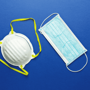 A white N95 mask with yellow straps and a blue surgical mask against a blue background