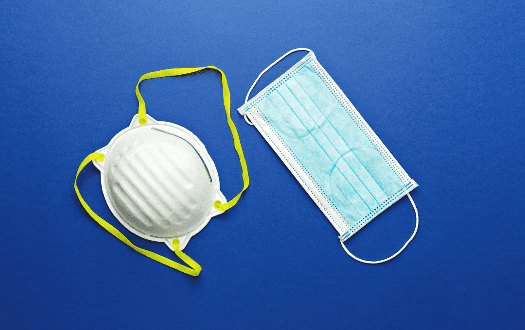 A white N95 mask with yellow straps and a blue surgical mask against a blue background